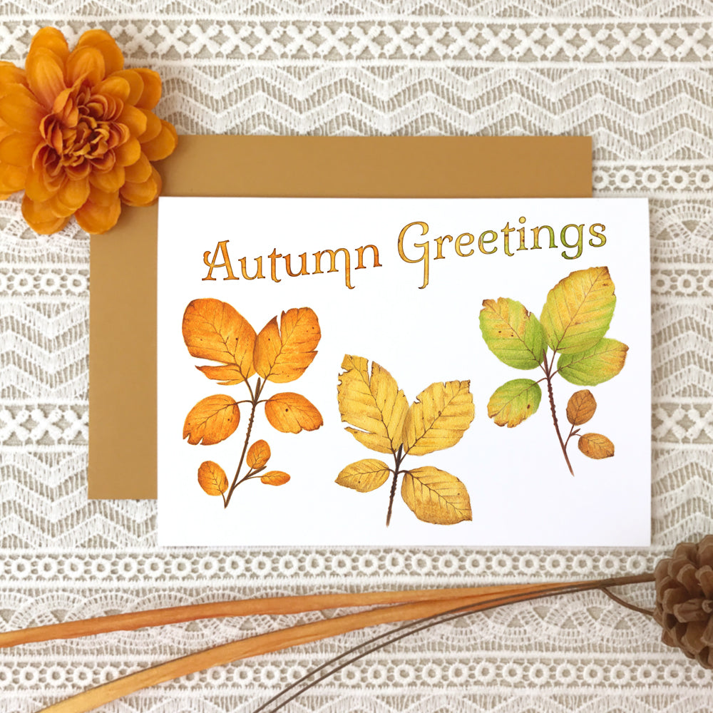 Fall greeting card with watercolor paintings of three beech leaves in orange, gold and green and the title "Autumn Greetings"