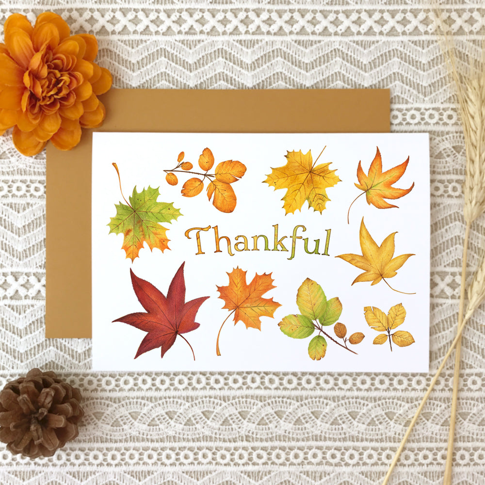 Thanksgiving greeting card with a collage of watercolor painted fall leaves surrounding the title, "Thankful".